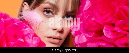 woman with feather on cheek near pink flowers isolated on orange, banner Stock Photo