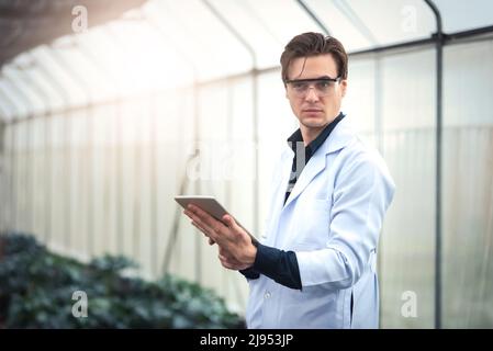 Portrait of handsome agricultural researcher holding tablet while working on research at plantation in industrial greenhouse Stock Photo