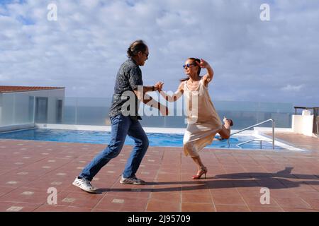 A middle-aged couple practice dancing the tango by a swimming pool. Stock Photo
