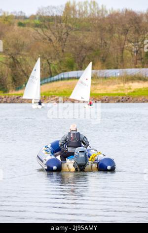 Safety officer in a powerboat out on a lake checking the safety on the water of sailing boat occupants Stock Photo