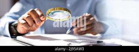 Close-up Of A Businessperson's Hand Holding Magnifying Glass Over Invoice At Workplace Stock Photo