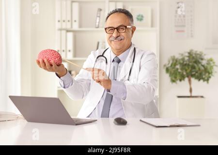 Mature male doctor sitting in an office and showing a brain model Stock Photo