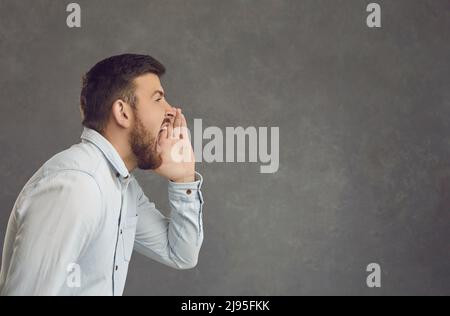 Side profile portrait of a man on a gray background who shouts announcing promotional information. Stock Photo
