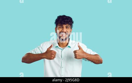 Portrait of happy cheerful young Indian man in shirt showing thumbs up and smiling Stock Photo