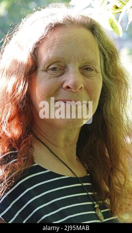 Portrait of a smiling elderly lady without make-up. Her hair is mixed coloured: grey and red. She has wrinkles in her face and is wearing a striped sh Stock Photo
