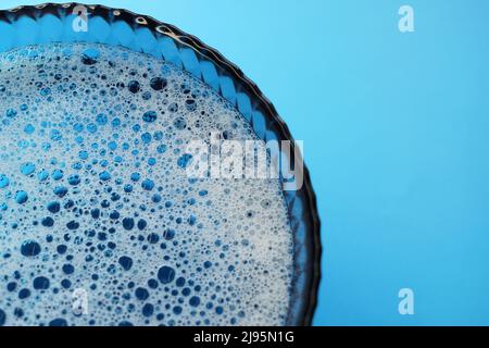 Glass bowl with foamy water and bubbles bursting on a blue table. Stock Photo