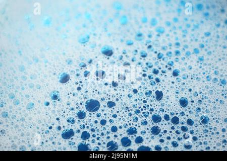 White foam with bubbles popping in blue water. Stock Photo