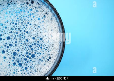 Glass bowl with foamy water and bubbles bursting on a blue table, copy space. Stock Photo