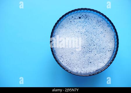 Glass bowl with foam water and bubbles on a blue table, copy space. Stock Photo