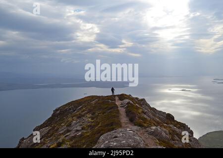 Hikers/hill walkers in silhouette on Ben Mor Coigach, a ridge near Ullapool, north west Scotland, Assynt, admire views of Summer Isles on a spring day Stock Photo