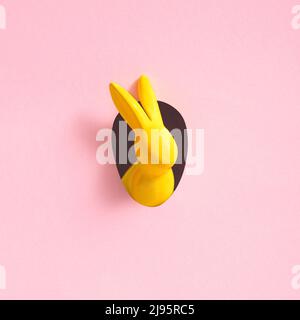 Yellow Easter bunny looks out of an egg-shaped hole in the pink background wall. Abstract concept. Square with copy space. Stock Photo