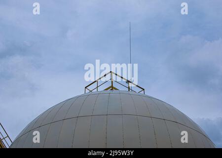 Round container for storing sunflower oil against the backdrop of a cloudy blue sky. Industrial landscape concept. Stock Photo