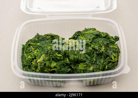 Boiled spinach in transparent food grade plastic box for refrigeration or storage, on light gray background Stock Photo