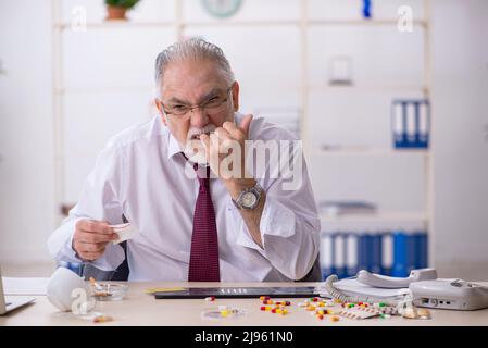 Old male drug addicted employee sitting at workplace Stock Photo