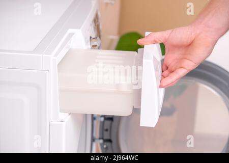 A man takes out a container from the dryer to collect water squeezed out of wet laundry. Stock Photo