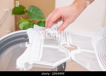 A man takes a lint filter out of the dryer and cleans it from dust, lint, hair, wool. Stock Photo