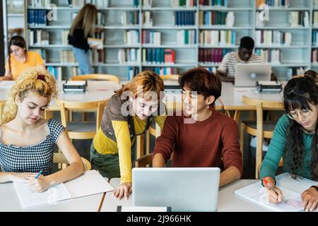 Young university students using laptop and studying with books in library - School education concept Stock Photo