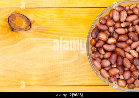 Roasted peanuts in a cup with copy space for text and advertising. Nut peanuts in a peel in a transparent bowl on a wooden textured table. The best Stock Photo
