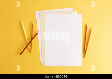 Colorful pencils and empty white papers . Empty place for text or drawing on the yellow background. Stock Photo