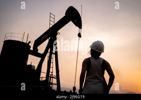 silhouette Petrochemical engineering asian woman with safety helmet standing in oil refinery structure petrochemical industry. Stock Photo