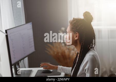 Beautiful mixed-race female coder working on new project texting on computer in apartment Stock Photo