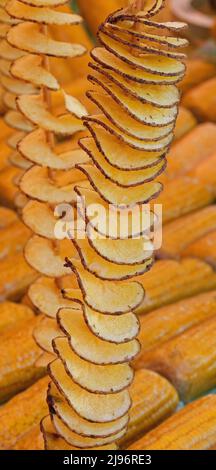 long skewers of fried potato chips with peel and yellow organic corn cobs  for sale in street food stall Stock Photo