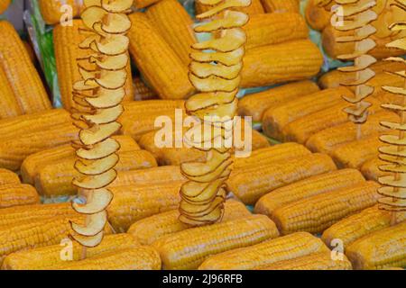 yellow cooked organic corn cobs with plastic wrap for sale in the street food stall and long fried potato skewers Stock Photo