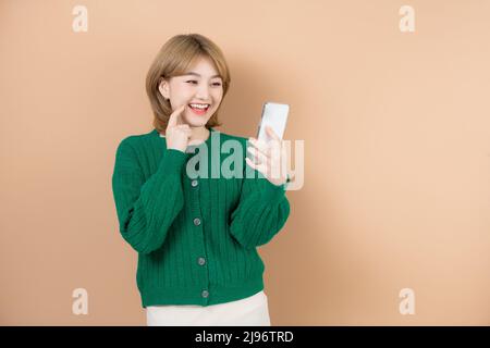 Smiling attractive young woman using mobile phone while standing isolated over beige background Stock Photo