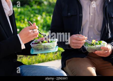 hands of two people eating a salad in a park Stock Photo