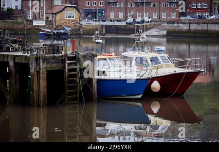 Moored red and blue boats at wooden quayside with water reflections in landscape.   Whitby 16052022 Stock Photo