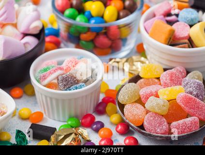 Jelly sugar gums candies on blue table with liquorice allsorts and strawberry marshmallow and large variety of sweets and candies. Stock Photo
