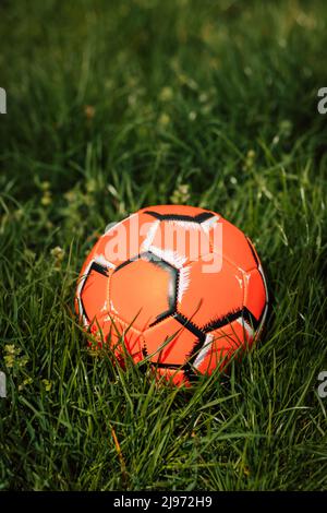 A bright orange soccer ball lies in the thick green grass Stock Photo