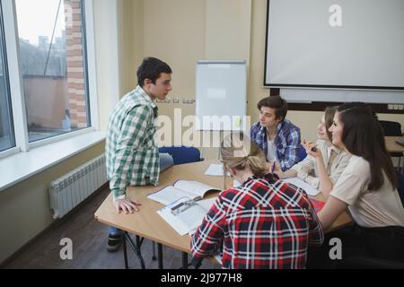 Male student sitting on a table, talking to his classmates during class at college Stock Photo
