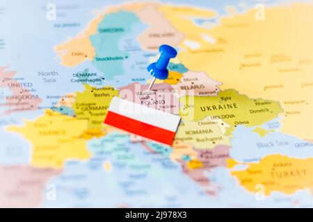 Blue push pin pointing at Poland together with a Polish flag on a political world map