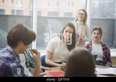 Happy college students and their teacher listening to a classmate talking Stock Photo
