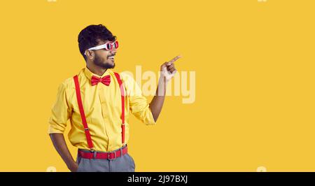 Happy young Indian man points to side to show something on yellow copy space background Stock Photo
