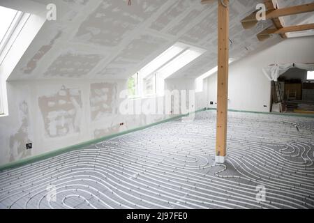 Shot of construction site in a loft where underfloor heating has just been installed, white pipes on grey mat Stock Photo