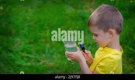 The child examines the water with a magnifying glass in a glass. Selective focus. Kid. Stock Photo