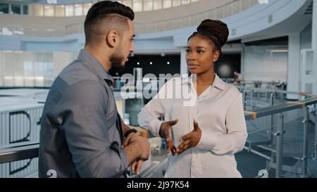 African American woman and Arabian Indian businessman talking in loft office hall working break diverse colleagues discussing news project in casual Stock Photo