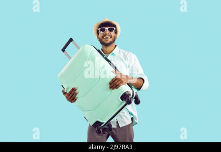 Happy Indian man who is going on holiday trip abroad is holding his suitcase and smiling Stock Photo