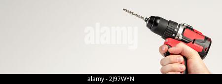 Cordless drill in black and red. Screwdriver with a drill in hand on a white background. Modern carpentry tool. Stock Photo