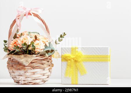 Fresh pink flowers in a basket and a box with a gift on the table with copy space. Stock Photo