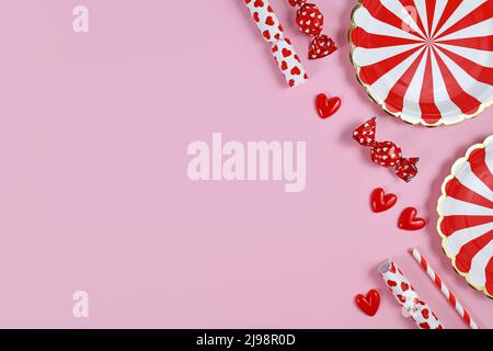 Party flat lay with red paper plates, heart ornaments, candy and drinking straws on pink  background with copy space Stock Photo