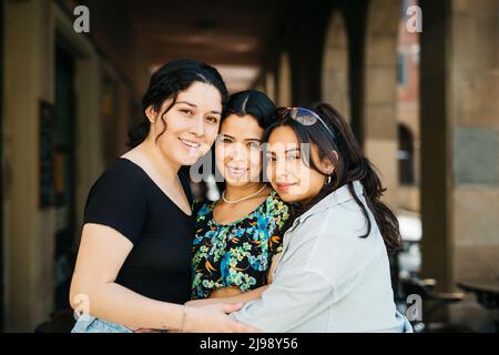 Three young latin american women embracing on the street Stock Photo