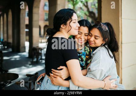 Three young latin american women embracing on the street Stock Photo