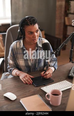 Vertical high angle view portrait of young woman drawing something using graphic tablet during live stream Stock Photo