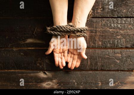 tied an old woman's hands with a rope on a wooden table, lack of will power over people, slave Stock Photo