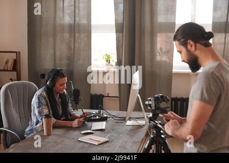 Horizontal selective focus shot of modern male videographer shooting video of young female blogger in loft room, copy space Stock Photo