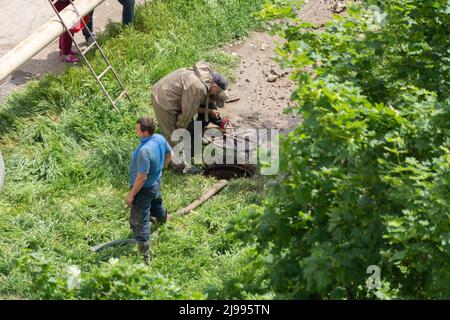 Tiraspol, Moldova - May 17, 2022: Male workers fixes a break in a water supply and sewerage pipe. Accident on the line of urban infrastructure. Poor q Stock Photo