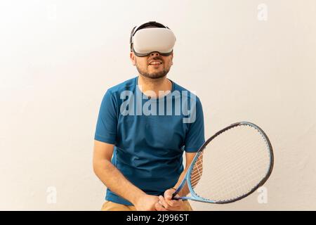 Man in position to play online tennis with a friend on his virtual reality goggles indoors. Stock Photo